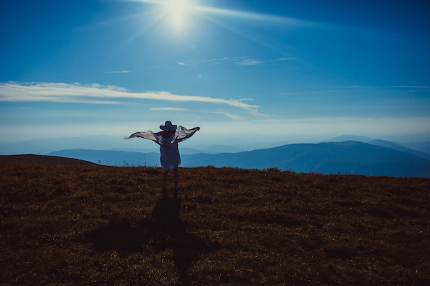 Chica joven con un pañuelo levantado, disfrutando de la luz del sol en la cima de la montaña