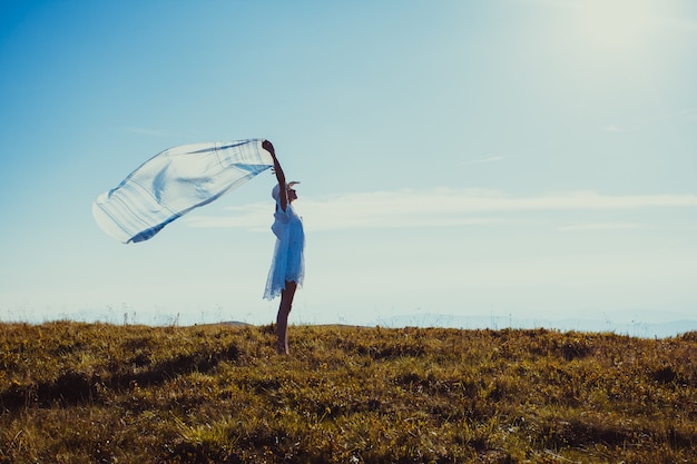 Chica joven con un pañuelo levantado, disfrutando de la luz del sol en la cima de la montaña