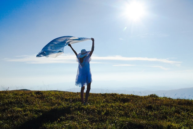 Chica joven con un pañuelo levantado, disfrutando de la luz del sol en la cima de la montaña