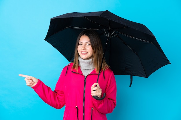 Chica joven con un paraguas sobre la pared azul