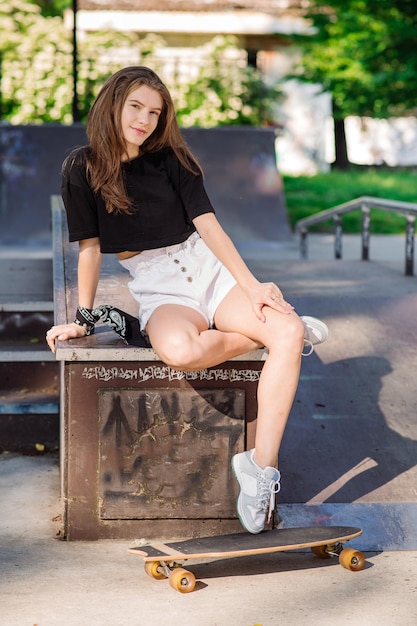 Chica joven patinadora descansando con una patineta en el parque de patinadores