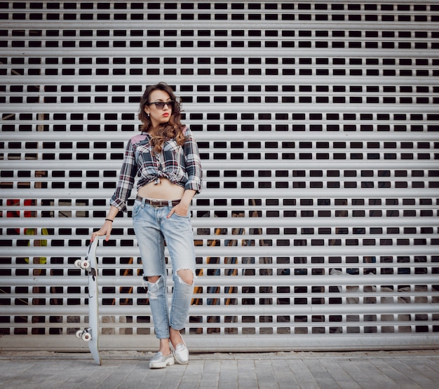 Chica joven con patineta en el de la gran pared gris.