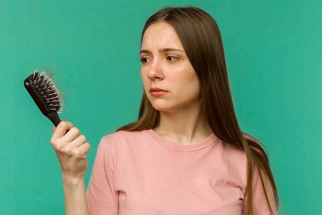 Chica joven con un peine y cabello problemático sobre fondo azul.