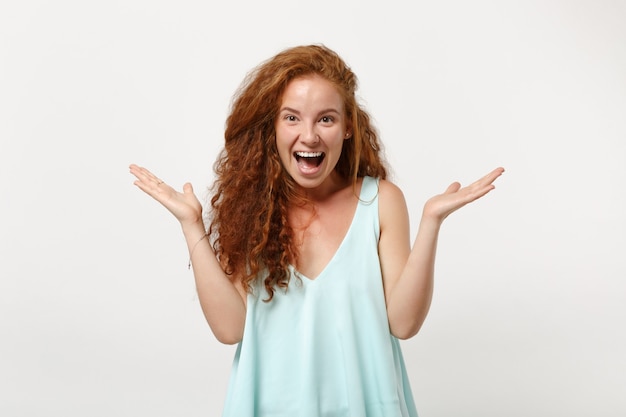 Chica joven pelirroja emocionada alegre en ropa ligera casual posando aislada sobre fondo blanco, retrato de estudio. Concepto de estilo de vida de personas. Simulacros de espacio de copia. Manteniendo la boca abierta, extendiendo las manos.