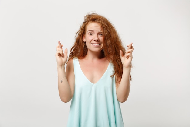 Chica joven pelirroja en ropa casual ligera posando aislada sobre fondo blanco. Concepto de estilo de vida de personas. Simulacros de espacio de copia. Esperando un momento especial, manteniendo los dedos cruzados, pidiendo deseos.