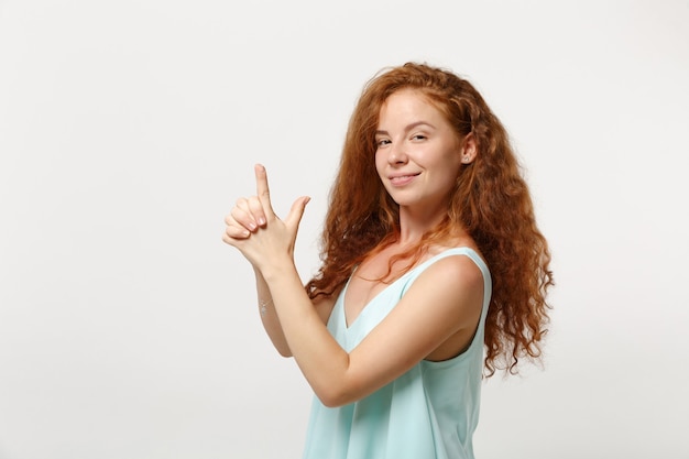 Chica joven pelirroja sonriente en ropa ligera casual posando aislada sobre fondo blanco, retrato de estudio. Concepto de estilo de vida de emociones sinceras de personas. Simulacros de espacio de copia. Tomados de la mano como una pistola.