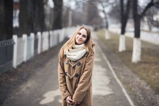 Chica joven de pelo rubio alegre alegre vestida con un abrigo beige y una bufanda blanca