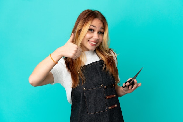 Foto chica joven peluquero sobre fondo azul aislado dando un gesto de pulgar hacia arriba