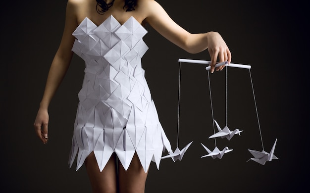 Chica joven pensativa con un vestido de origami tiene un pájaro de origami en sus manos.