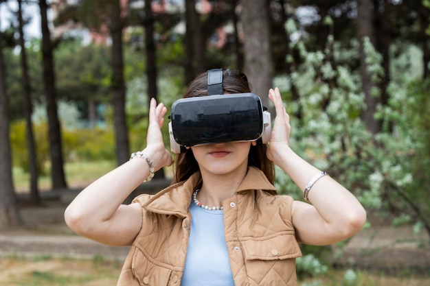 Chica joven de pie en el bosque y usando un set de realidad virtual