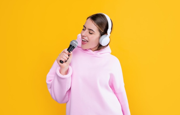 Chica joven positiva en auriculares con micrófono sobre fondo amarillo