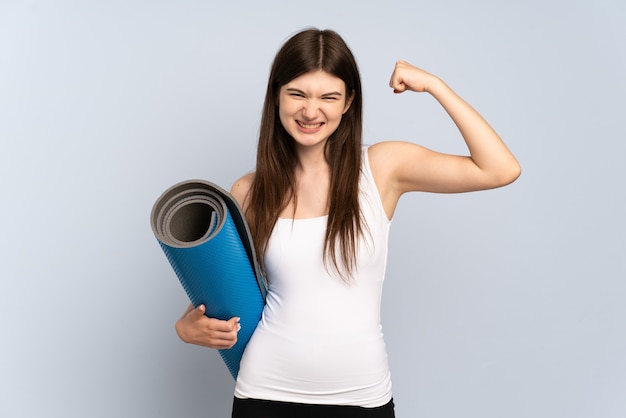 Chica joven que va a clases de yoga mientras sostiene una estera haciendo un gesto fuerte