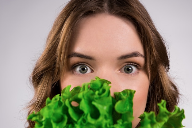 Chica joven que se esconde detrás de las hojas de lechuga.