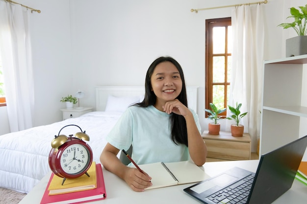 Chica joven que estudia con la computadora portátil en el dormitorio aprendiendo en casa