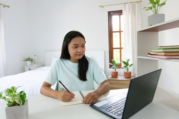 Chica joven que estudia con la computadora portátil en el dormitorio aprendiendo en casa