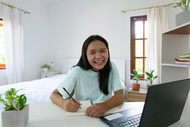 Chica joven que estudia con la computadora portátil en el dormitorio aprendiendo en casa