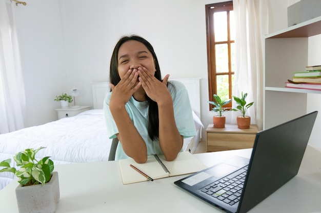 Chica joven que estudia con la computadora portátil en el dormitorio aprendiendo en casa