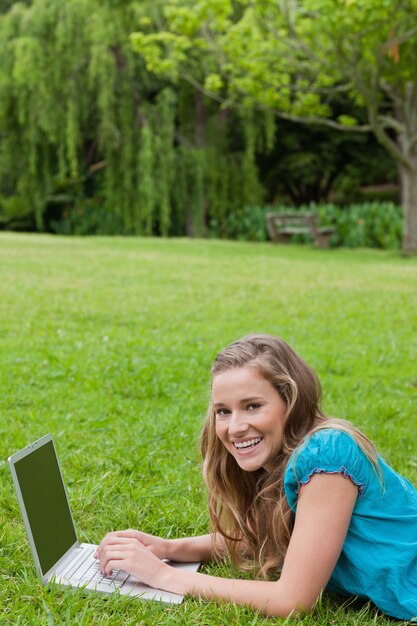 Chica joven que ríe mientras que mecanografía en su computadora portátil