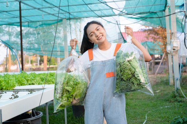 Chica joven que sostiene una bolsa grande de verduras en la granja hidropónica