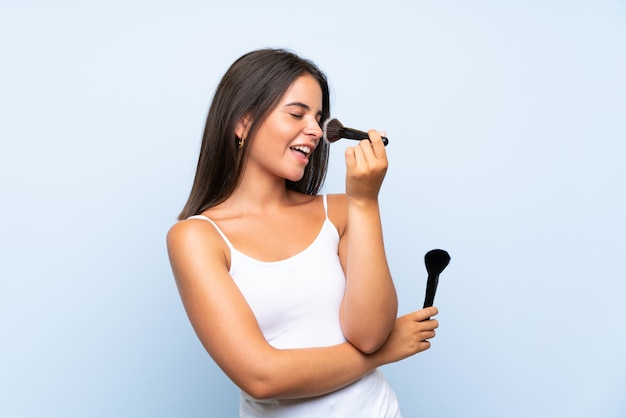 Chica joven que sostiene el cepillo del maquillaje sobre la pared aislada