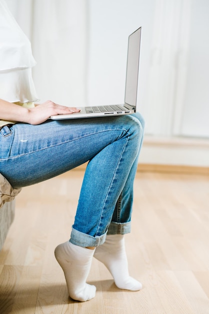 Chica joven que sostiene la computadora portátil en sus piernas y se sienta en el entrenador