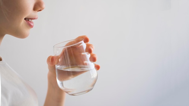 Chica joven que sostiene un vaso de agua en sus manos