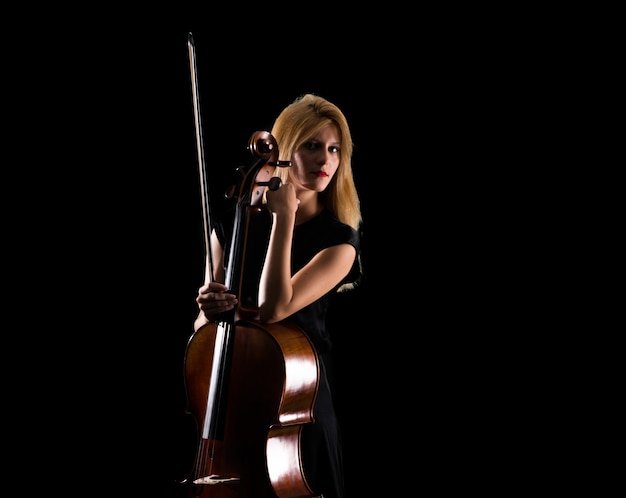 Chica joven que toca el violoncelo en fondo negro aislado