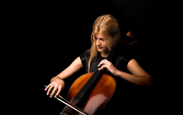 Chica joven que toca el violoncelo en fondo negro aislado