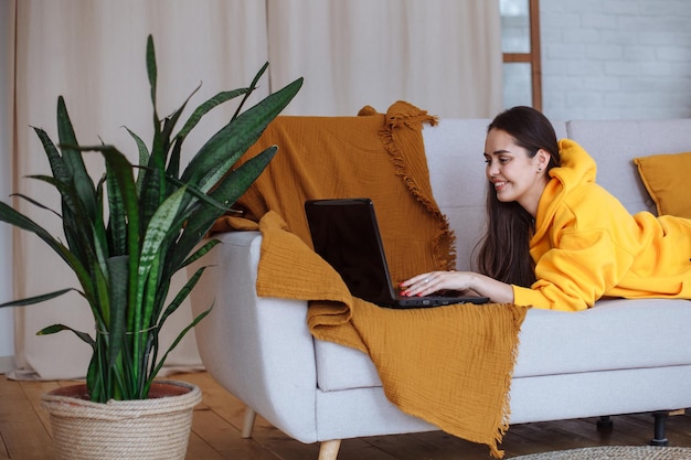 Chica joven que trabaja en casa en el sofá con una computadora portátil