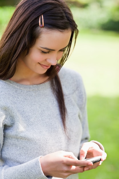 Chica joven relajada que envía un texto con su teléfono móvil mientras que se coloca en un parque