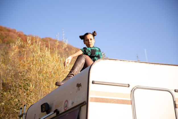 Chica joven relajándose en el techo de una autocaravana retro en la montaña. Atmósfera otoñal