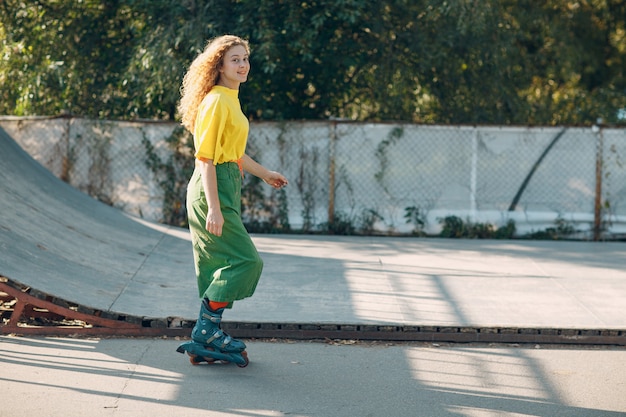 Chica joven en ropa verde y amarilla y medias naranjas con patinaje sobre ruedas peinado rizado en el parque de patinaje