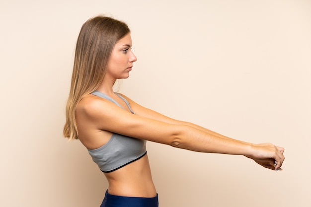 Chica joven rubia deporte sobre estiramiento de pared aislada