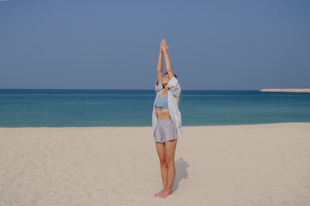 Chica joven rubia practica yoga y meditación en la pose de Surya namaskar asana en la playa en un día soleado.