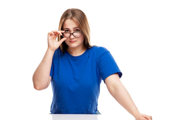 Chica joven seria en una camiseta azul ajusta sus gafas. Educación y conocimiento. .