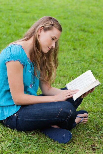 Chica joven seria leyendo un libro mientras estaba sentado en un parque