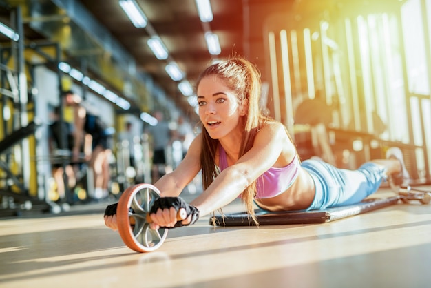 Chica joven sexy fuerte ejercitándose en un gimnasio brillante.