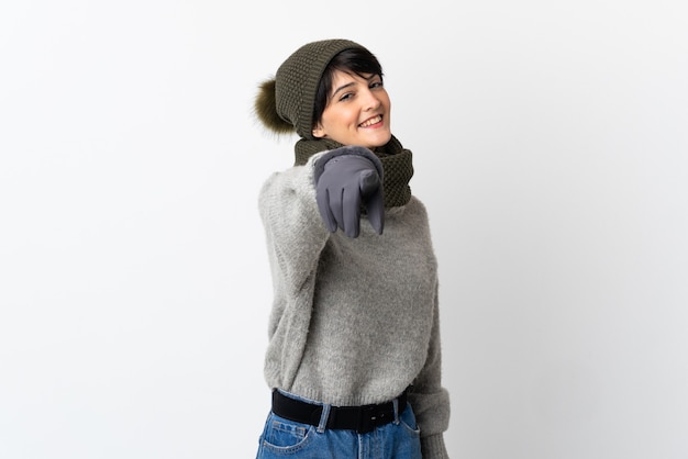 Chica joven con sombrero de invierno apuntando al frente con expresión feliz