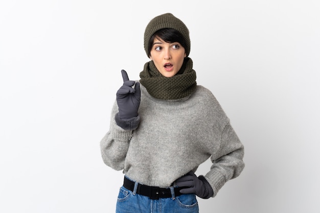 Chica joven con sombrero de invierno pensando en una idea apuntando con el dedo hacia arriba