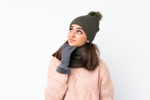 Chica joven con sombrero de invierno sobre blanco aislado pensando en una idea