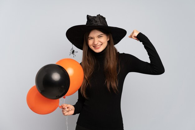 Chica joven con sombrero negro y vestido negro sosteniendo globos