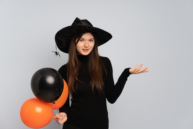 Chica joven con sombrero negro y vestido negro sosteniendo globos