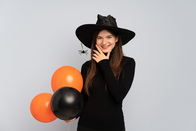 Chica joven con sombrero negro y vestido negro sosteniendo globos