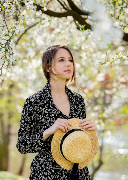 Chica joven con un sombrero permanecer cerca de un árbol en flor en el parque. Temporada de primavera