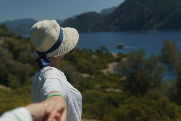 Chica joven con sombrero sosteniendo la mano de un hombre desconocido y llamándolo para disfrutar de la hermosa naturaleza y ...