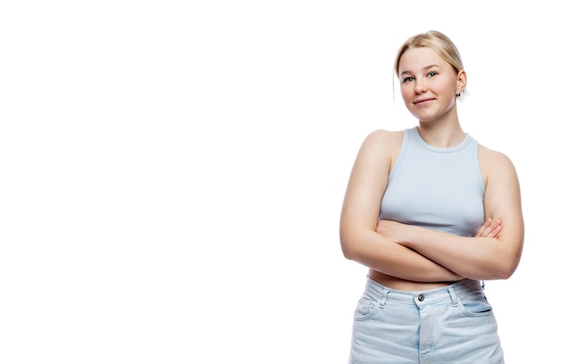 Chica joven sonriente Una linda adolescente rubia con un top azul y jeans se encuentra con los brazos cruzados sobre el pecho aislado en un fondo blanco Espacio para texto