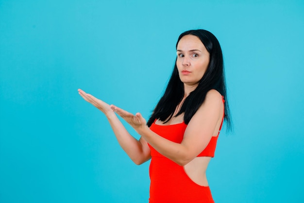 Chica joven sorprendida está levantando sus puñados sobre fondo azul.