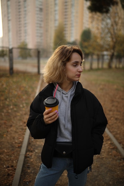 La chica joven sostiene un vaso de café en la mano. chica bebe un café de un vaso de papel en la calle