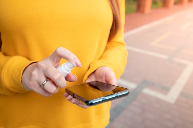 Chica joven con un suéter amarillo tiene un teléfono inteligente en la calle