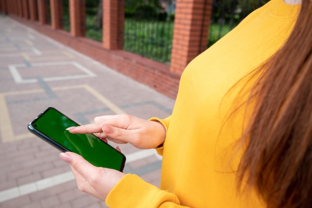 Chica joven con un suéter amarillo tiene un teléfono inteligente en la calle